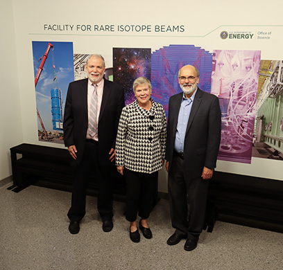 Pictured, from left: Sherman Garnett, former dean of MSU’s James Madison College, Rose Gottemoeller, and FRIB Scientific Director Bradley M. Sherrill. They are standing in front of a mural of photos from around the FRIB Laboratory.